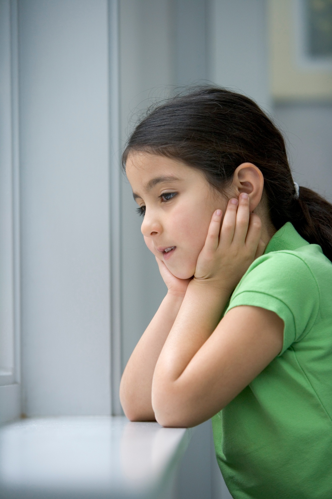 Little girl is looking out of the window with a sad face